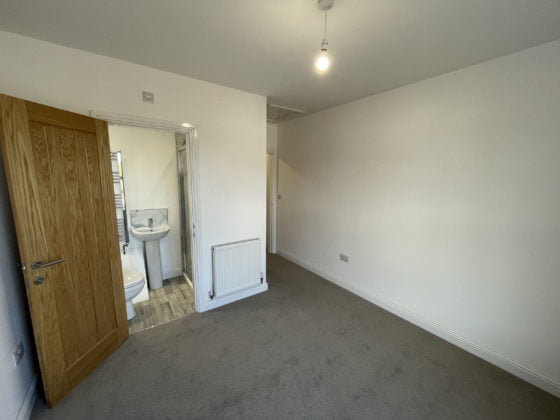 Empty room with open bathroom door and grey carpet.