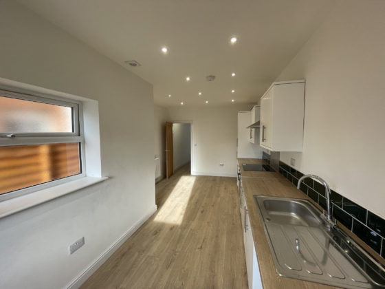 Modern kitchen interior with wooden flooring and white cabinets.