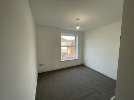 Empty room with window, pendant light, and gray carpet.