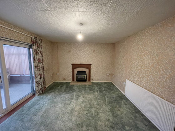 Empty living room with fireplace and patterned wallpaper.