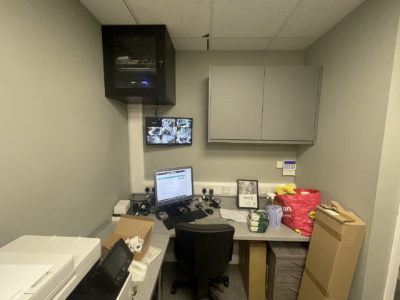 Office space with computer, CCTV monitors, and clutter.