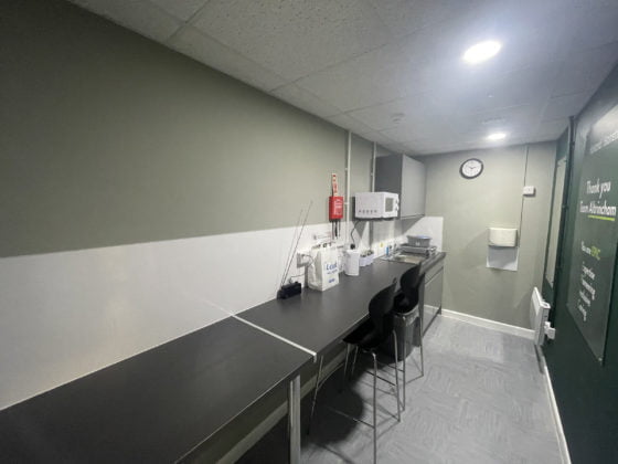 Modern office kitchenette with clock and appliances.