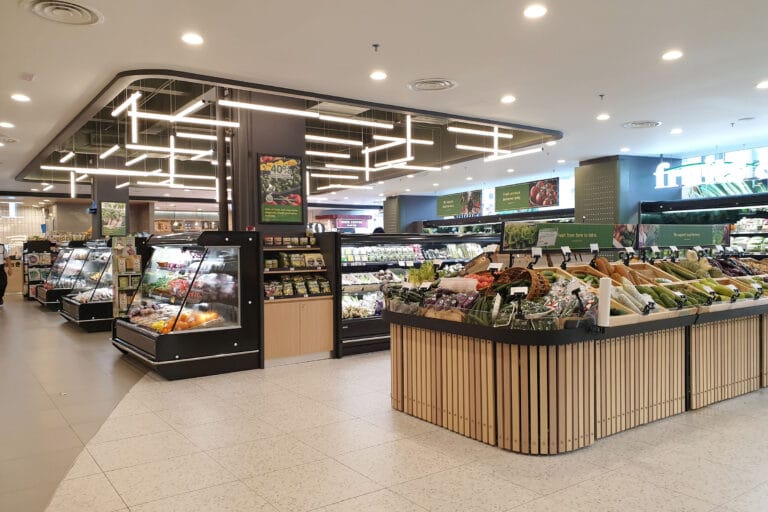 Well-lit supermarket produce section with various vegetables.