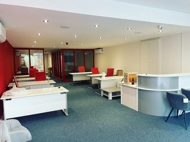 Modern office with red chairs and white desks.