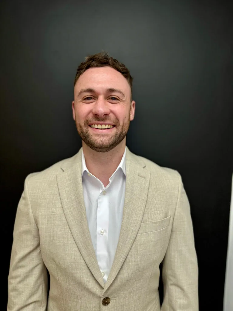 Smiling person in beige suit against black background